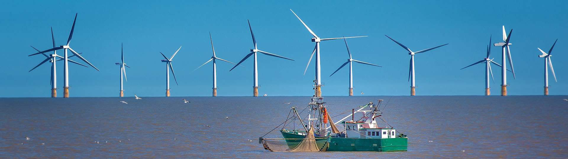 Image of fishing troller on ocean with wind turbines in the background